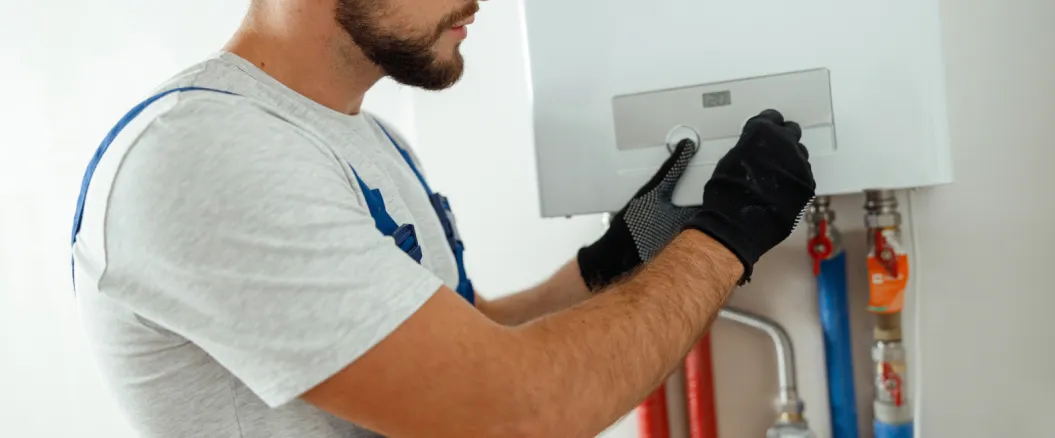 Technician adjusting the settings on a water heater or boiler unit while wearing black gloves.