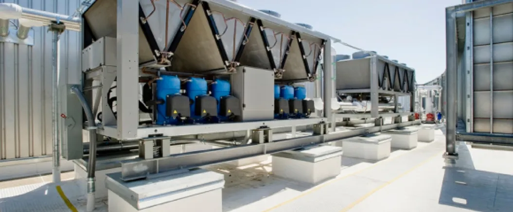 Large industrial HVAC cooling units installed on a rooftop with visible compressors and connected piping systems.