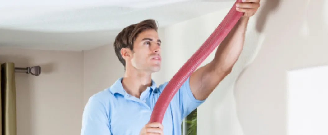 Technician holding a red hose while cleaning or inspecting an air duct in a residential ceiling.