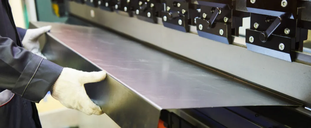 Worker in gloves operating a sheet metal bending machine in an industrial setting.