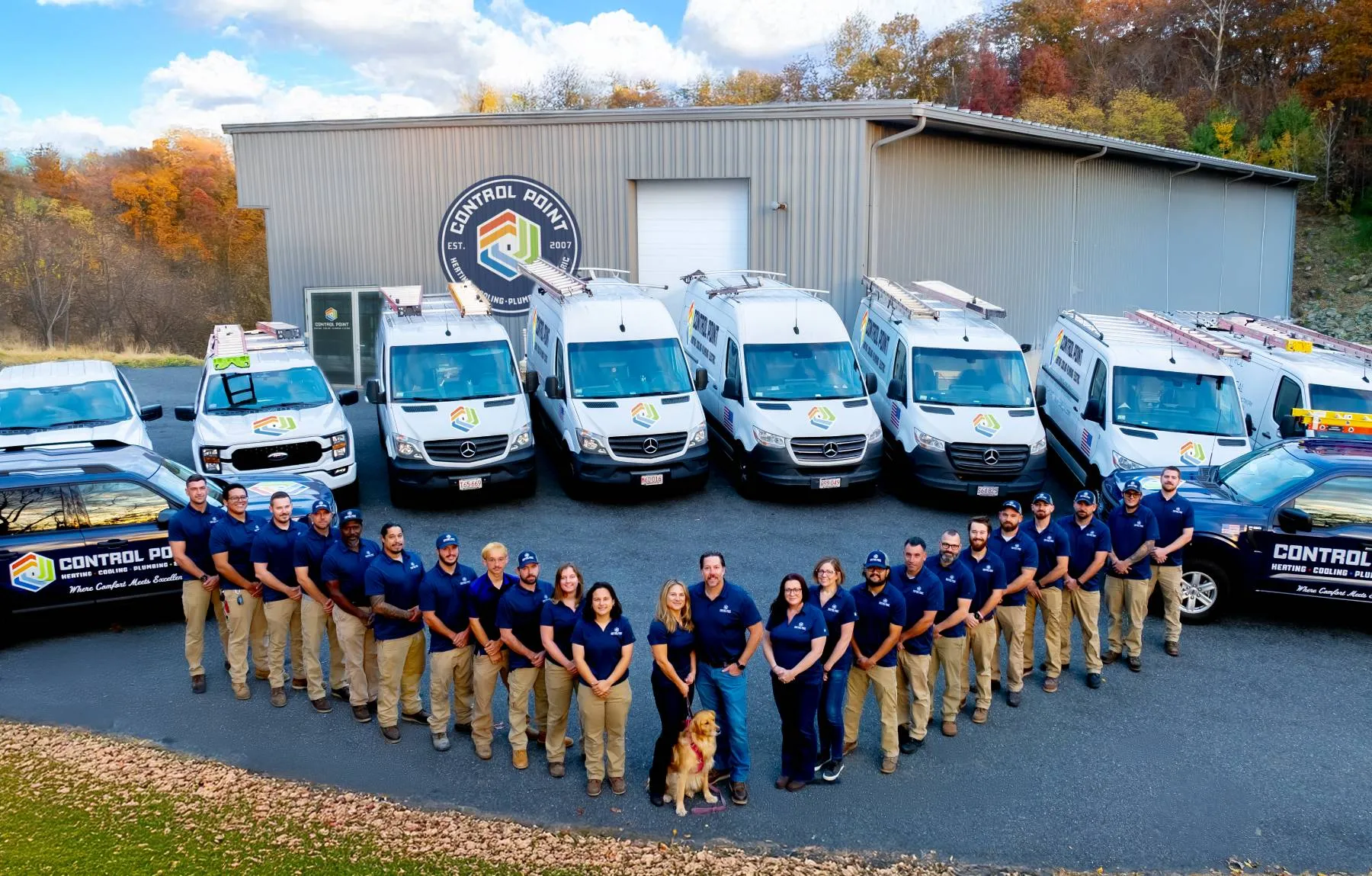 Team of HVAC professionals standing in front of their company vehicles and headquarters, branded with the "Control Point" logo.